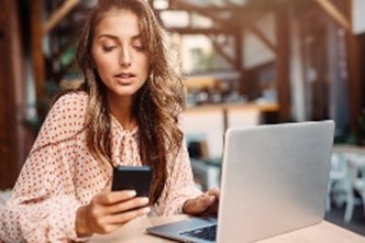 A woman using a smartphone and a laptop.