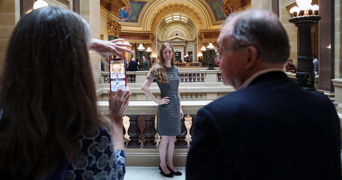 a person poses for a photo while another holds up a cell phone