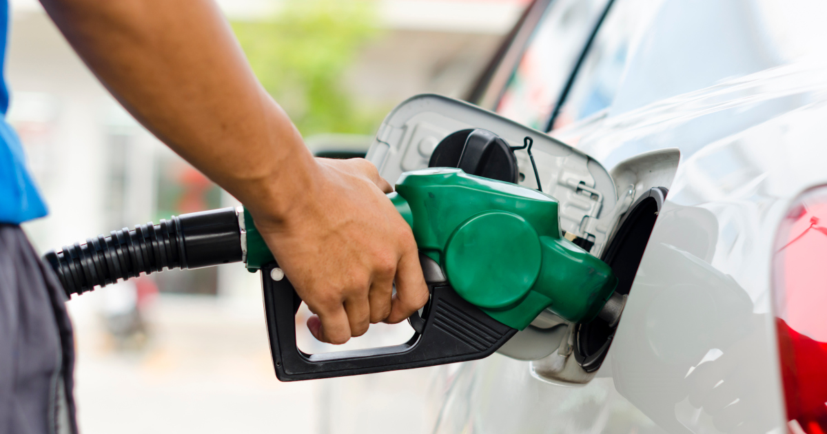 Medium Close Up Of Man's Arm, Reaching In From The Left Side Of The Frame, Instering A Green Handled Gas Nozzle Into The Gas Tank Of A White Sedan