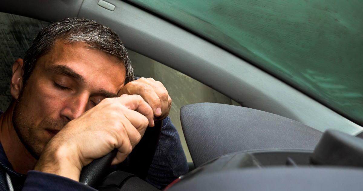 On The Left Side Of The Frame, A 40 Something Man Grips The Steering Wheel Of A Pickup Truck, Leaning His Head Down On His Hands With His Eyes Closed