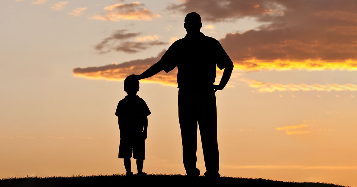 father and son silhouetted stand looking into the distance